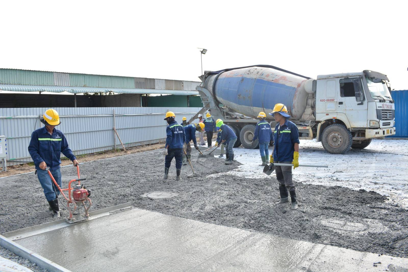 Construction crew spreading fresh concrete beside a mixer truck (stock photo)